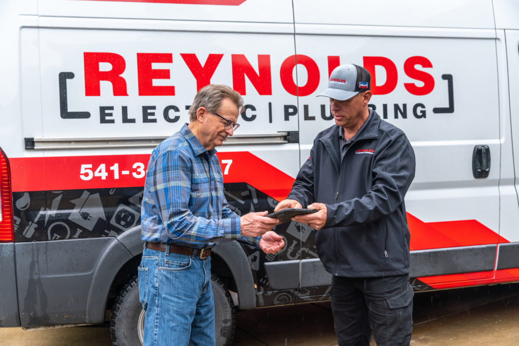 Electrician discussing with male customer in front of a Reynolds Electric and Plumbing van.