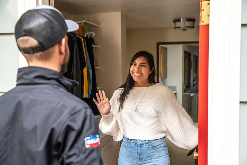 Woman smiling and greeting a Reynolds Electric and Plumbing technician at her front door.