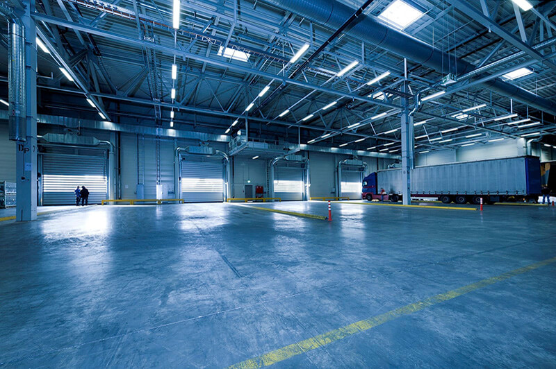 An largely empty warehouse with a semi truck and two people in the distance.