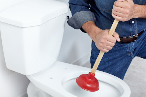 A man holding a plunger over a toilet bowl.