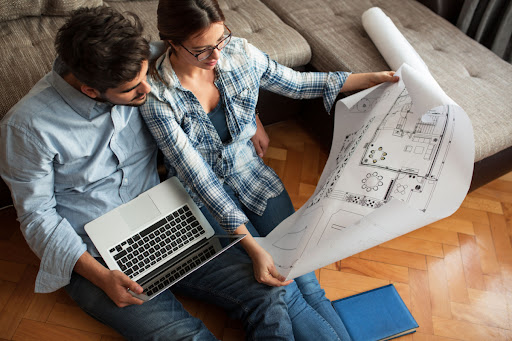 A couple looking at blueprints for a house while holding a laptop.