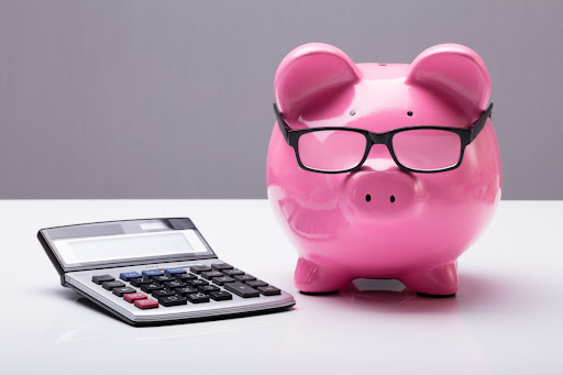 A piggy bank with glasses next a a calculator on a white surface.