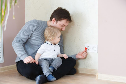 Toddler sitting on dad's lap, who is installing an outlet plug.