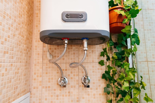 Tankless water heater installed on side of home with plant hanging next to it.