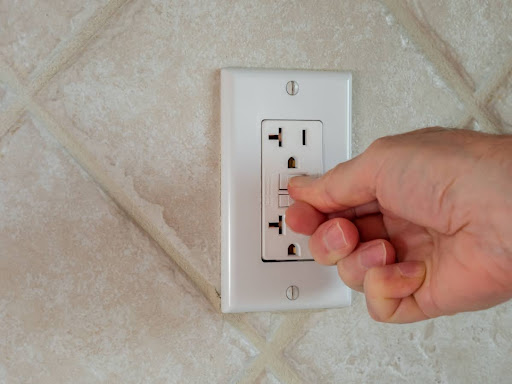 A close-up of a hand resetting a GFCI outlet on a wall.