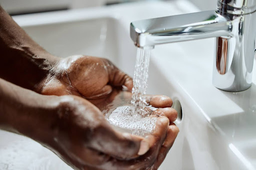 A man cupping water in his hands as it flows from a sink.