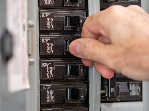 A close-up of a hand resetting a circuit breaker on an electrical panel.